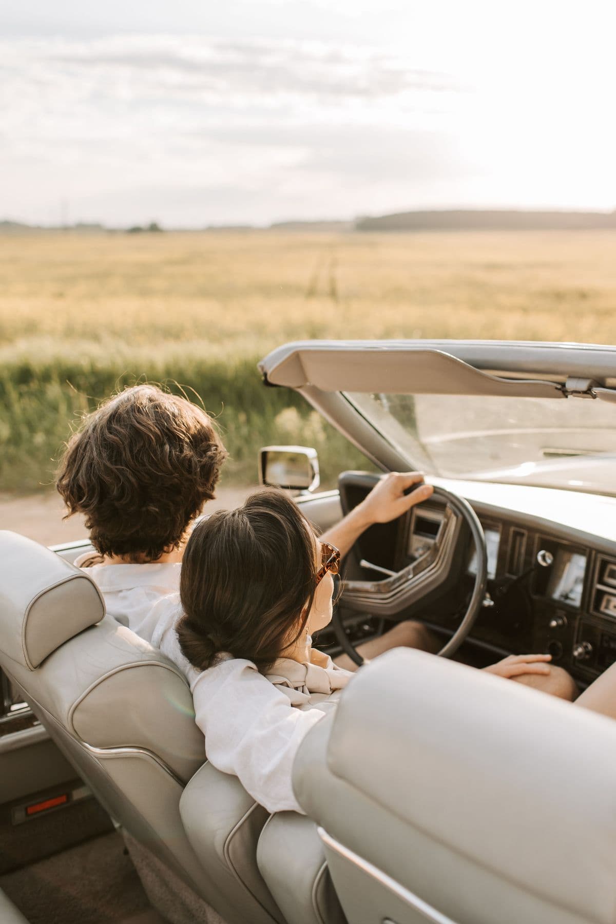 Two people driving a convertible through open countryside at golden hour